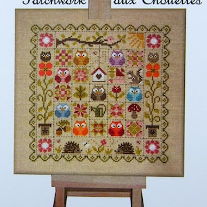 Peut inclure: Broderie au point de croix avec un motif patchwork représentant des hiboux, des fleurs et des éléments naturels. L'échantillon est présenté sur un chevalet en bois. Le texte "Patchwork aux Chouettes" est en haut.