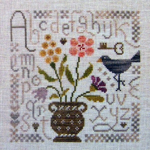 Peut inclure: Modèle de point de croix avec un pot de fleurs brun contenant un bouquet de fleurs, un oiseau et une clé. L'alphabet est brodé autour du motif.