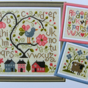 Peut inclure: Modèle de point de croix représentant un arbre avec un oiseau et des maisons, un mouton dans un champ et un tableau de l'alphabet. Le tableau de l'alphabet est dans un cadre rose, le mouton est dans un cadre bleu et l'arbre est dans un cadre marron.
