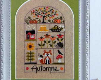 Può includere: Un ricamo a punto croce incorniciato che presenta una scena autunnale con una casa, un albero, una volpe, un riccio e un uccello. Il disegno è intitolato "Automne" in francese e "Autumn" in inglese.