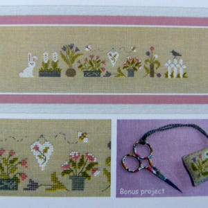 Peut inclure: Un motif de point de croix avec une rangée de plantes en pot, un lapin blanc et un oiseau sur une structure en nid d'abeille, le tout dans un cadre rose et beige. Comprend un gros plan du motif et des ciseaux décoratifs avec un petit carré brodé floral.