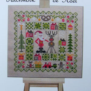 Könnte beinhalten: Ein Kreuzstichmuster auf einer Leinwand, das ein Patchwork-Design mit einem Weihnachtsmann und einem Rentier darstellt. Das Design enthält verschiedene Weihnachtssymbole wie Geschenke, Bäume und Häuser. Die Leinwand ist auf einem Holzstaffelei montiert. Der Text "Patchwork de Noël" ist oben im Bild sichtbar.