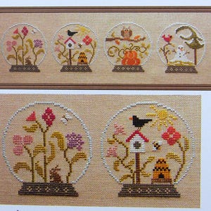 Peut inclure: Quatre motifs de point de croix de globes à neige avec des scènes différentes. Le premier globe à neige montre un nichoir avec un oiseau, une ruche et des fleurs. Le deuxième globe à neige montre un hibou perché sur une branche avec des citrouilles et des feuilles d'automne. Le troisième globe à neige montre un bonhomme de neige avec un oiseau et un arbre. Le quatrième globe à neige montre un nichoir avec un oiseau, une ruche et des fleurs.