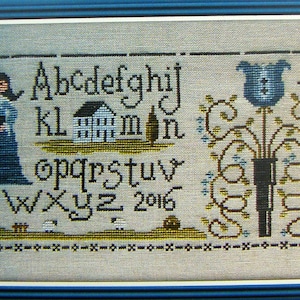 Peut inclure: Un sampler de point de croix avec une maison bleue, une femme en robe bleue, une fleur bleue et l'alphabet en noir. Le sampler est encadré dans un cadre bleu.