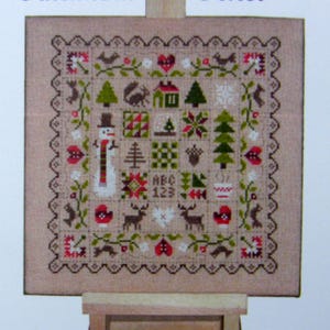 Peut inclure: Un modèle de point de croix sur un chevalet en bois avec un fond beige et une scène d'hiver colorée. Le motif est intitulé "Patchwork Hiver".