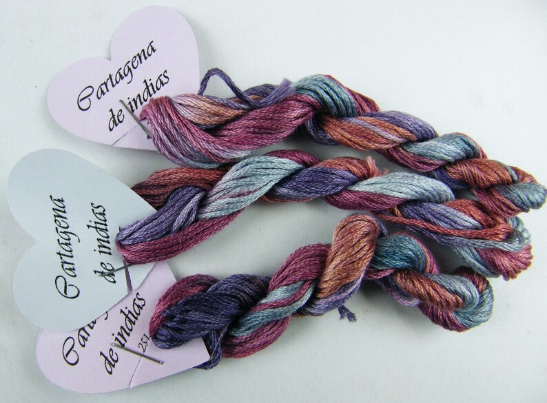 May include: Two skeins of embroidery floss in shades of purple, blue, and brown, labeled "Cartagena de Indias" on heart-shaped tags.