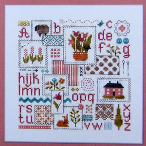 Peut inclure: Un sampler de point de croix présentant l'alphabet dans un design patchwork. Chaque lettre est entourée d'un motif différent, notamment des fleurs, une maison, un mouton et un oiseau. Le sampler est encadré d'une bordure rose.