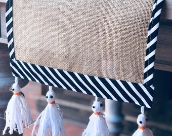 May include: A burlap table runner with black and white striped trim and white ghost-shaped tassels.