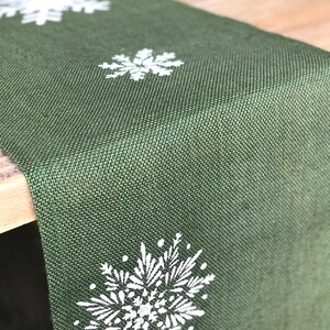 May include: A green burlap table runner with white snowflake designs.