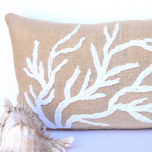 May include: A beige burlap pillow with a white embroidered coral design.