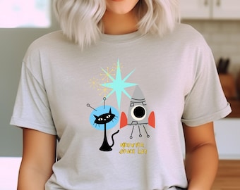 Może przedstawiać: Jasnoszara koszulka z grafiką w stylu retro. Projekt zawiera czarnego kota, rakietę i gwiazdę. Tekst "MEOWTER SPACE CAT" jest wydrukowany pod rakietą. Koszulka ma krótkie rękawy i okrągły dekolt.