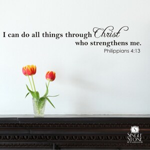 May include: A white wall with a black inspirational quote that reads "I can do all things through Christ who strengthens me. Philippians 4:13". Two red and yellow tulips are in a clear glass vase on a dark wood mantel.