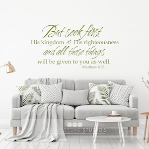 May include: A living room interior with a gray couch, two end tables, and a floor lamp. The wall behind the couch has a green vinyl decal with the text "But seek first His kingdom & His righteousness and all these things will be given to you as well. Matthew 6:33".