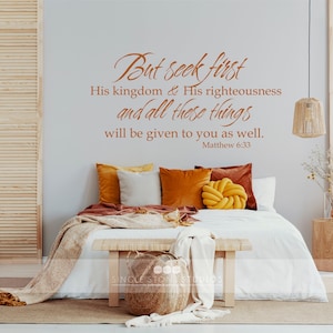 May include: A bedroom with a white bed, a wooden headboard, and a brown throw blanket. The wall behind the bed has a brown vinyl decal with the text "But seek first His kingdom & His righteousness and all these things will be given to you as well. Matthew 6:33".
