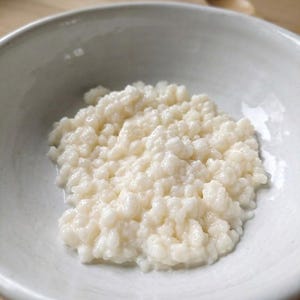 Puede incluir: Primer plano de un cuenco de cer&aacute;mica blanco lleno de una sustancia cremosa, blanquecina y granulada. La sustancia parece k&eacute;fir o un alimento fermentado similar. El cuenco est&aacute; sobre un fondo claro.