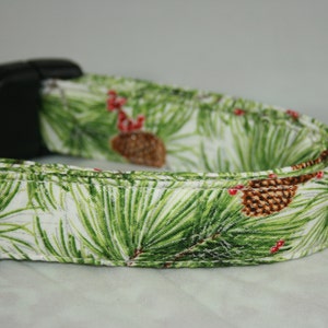 May include: A white dog collar with a green pine needle and red berry print. The collar has a black plastic buckle.