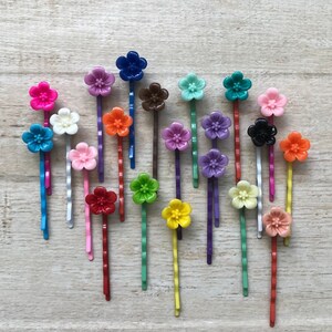 May include: A set of 20 colorful flower hair clips. The clips are made of plastic and have a variety of colors, including pink, red, orange, yellow, green, blue, purple, and black. The clips are all in the shape of a flower and have a small metal clip on the back.