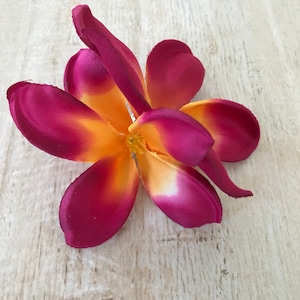 May include: A single, artificial plumeria flower with five petals. The petals are a deep burgundy color with a yellow center.