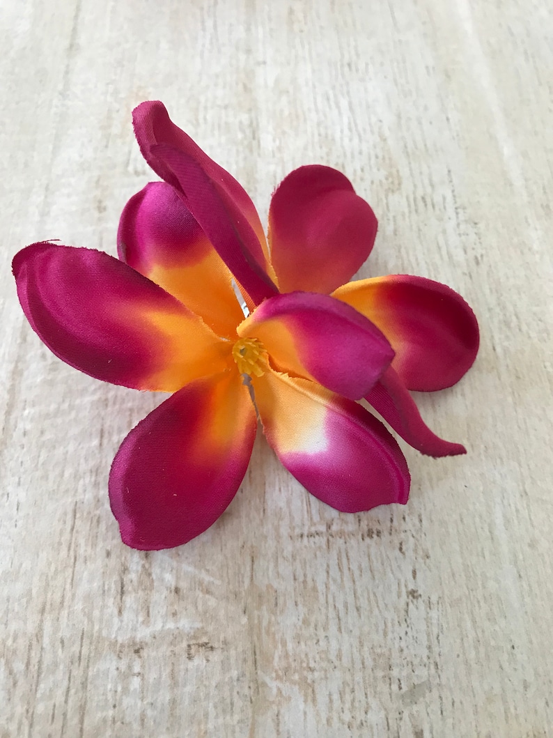 May include: A single, artificial plumeria flower with five petals. The petals are a deep burgundy color with a yellow center.