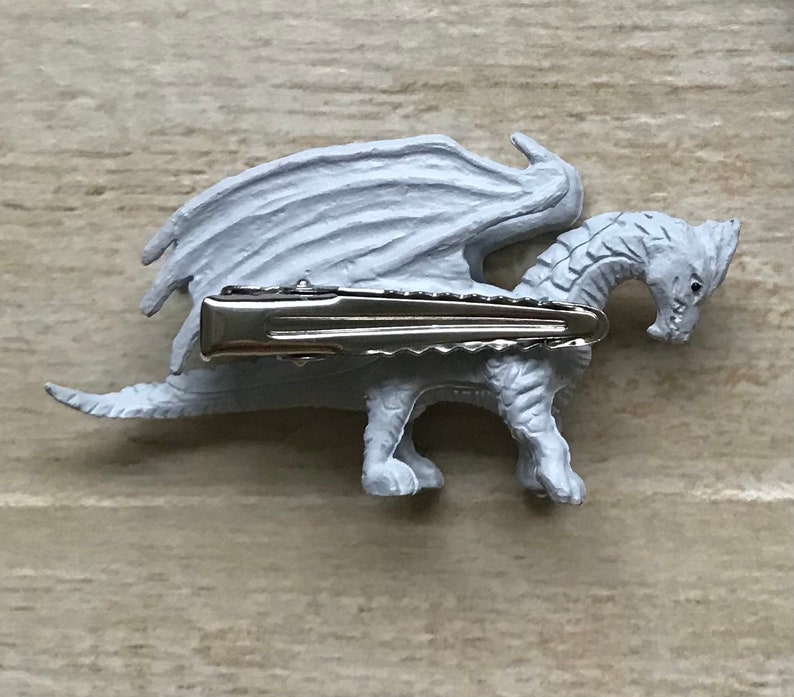 May include: A white dragon hair clip with a silver metal clip. The dragon has wings and a long tail.