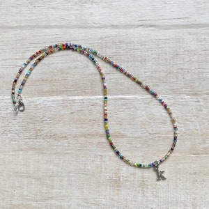 May include: A colorful beaded necklace with a silver letter K charm. The necklace is made of small, multi-colored beads and has a silver clasp.