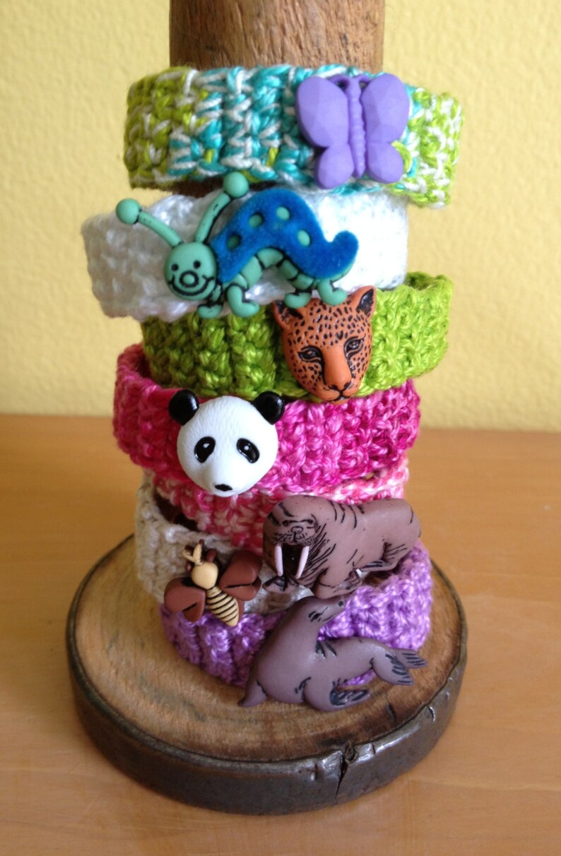 May include: A stack of colorful crocheted bracelets with various animal button embellishments, including a butterfly, ladybug, panda, jaguar, walrus, and seal.