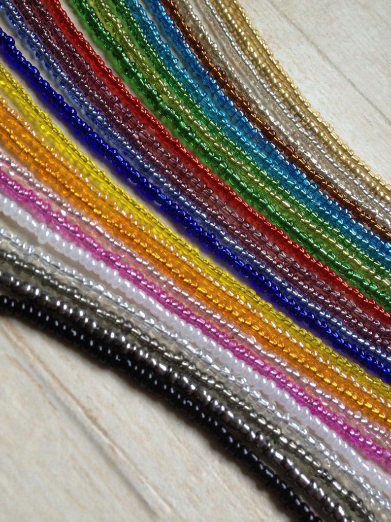 May include: A collection of 20 strands of seed beads in various colors, including black, white, silver, gold, pink, orange, yellow, green, blue, and purple.
