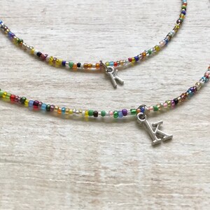 May include: Two colorful beaded necklaces with silver letter charms. The necklaces are layered and feature a variety of small, colorful beads.