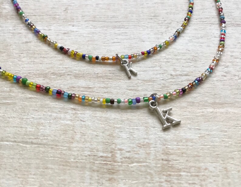 May include: Two colorful beaded necklaces with silver letter charms. The necklaces are layered and feature a variety of small, colorful beads.
