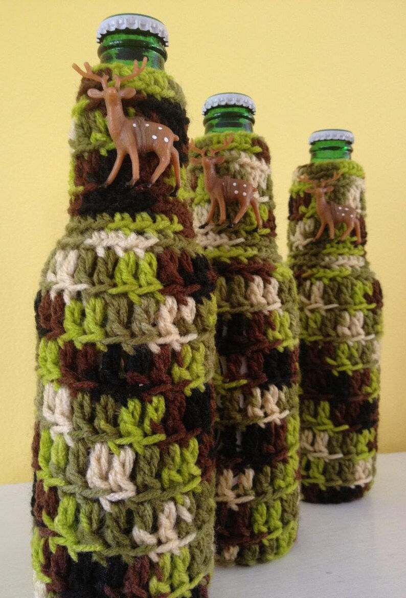 May include: Three glass bottles covered in crocheted camouflage fabric with small deer figurines attached to each bottle.