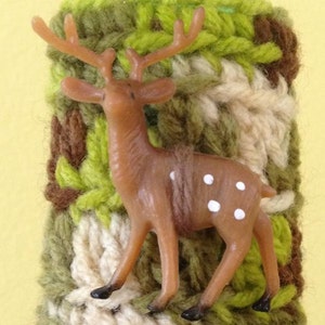 May include: A brown and white deer figurine with white spots, attached to a crocheted green, brown, and white fabric cuff.