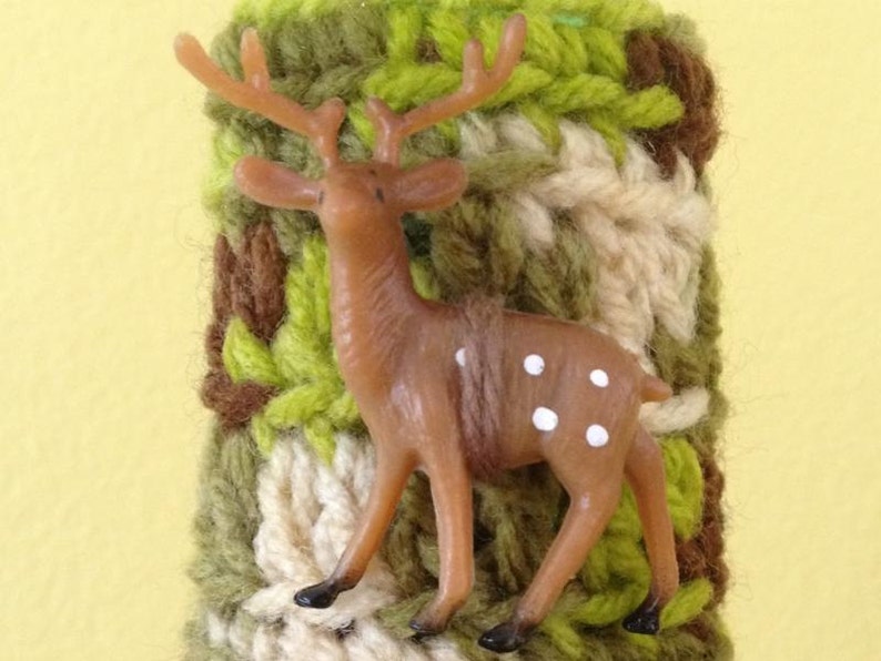 May include: A brown and white deer figurine with white spots, attached to a crocheted green, brown, and white fabric cuff.