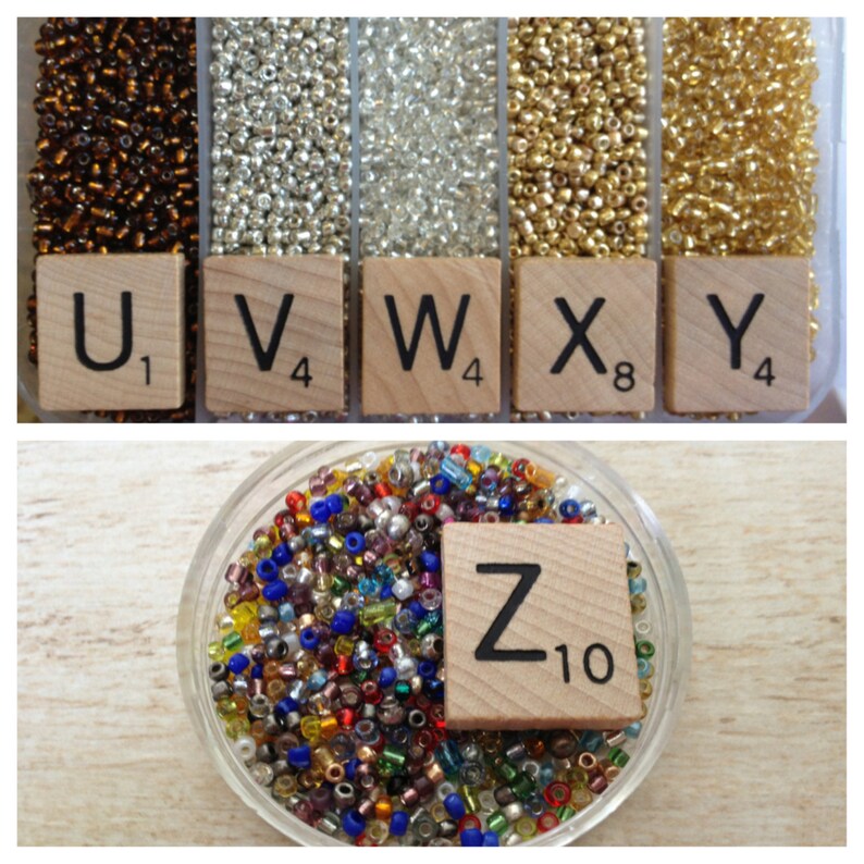 May include: Assortment of seed beads in various colors, including gold, silver, brown, and clear. The beads are displayed in small containers with letter tiles labeled U, V, W, X, Y, and Z. The letter tiles are from a Scrabble game.