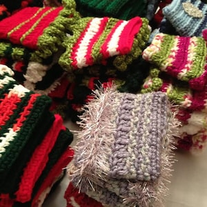 May include: A collection of colorful crocheted items, including hats, scarves, and other accessories. The items are made in a variety of colors, including red, green, white, and purple. Some of the items have a fluffy texture, while others are more smooth.
