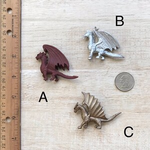 May include: Three miniature dragon figurines. The first dragon is brown with a red underbelly, the second is silver, and the third is gold. The dragons are posed in a flying position with their wings spread.