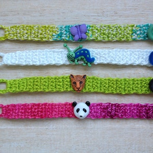 May include: Four crocheted bracelets with different colored buttons and charms. The bracelets are green, white, lime green, and pink. The charms include a butterfly, a caterpillar, a leopard, and a panda.