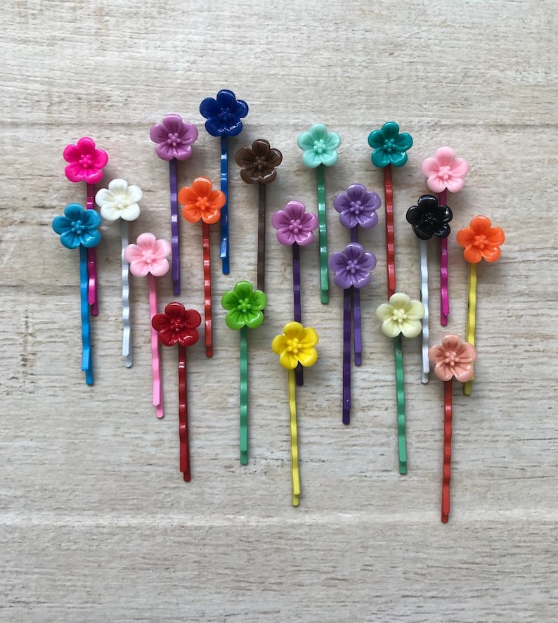 May include: A set of 20 colorful flower hair clips. The clips are made of plastic and have a variety of colors, including pink, red, orange, yellow, green, blue, purple, and black. The clips are all in the shape of a flower and have a small metal clip on the back.