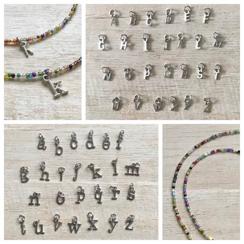 May include: A set of silver alphabet letter charms, each letter is on a separate charm. The charms are displayed on a wooden surface. There are two strands of colorful seed beads in the background.