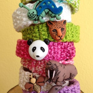 May include: A stack of crocheted bracelets with colorful buttons featuring a butterfly, caterpillar, leopard, panda, walrus, and seal.