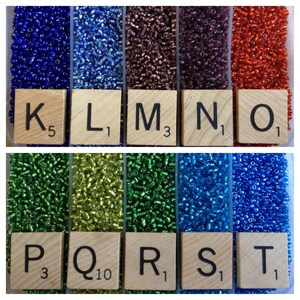 May include: A close-up of ten small containers filled with different colored seed beads. The containers are labeled with letters K through T and numbers indicating the quantity of beads in each container.