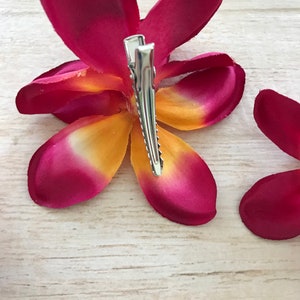 May include: A pink and yellow flower hair clip with a silver clip. The flower is made of fabric and has a realistic appearance.
