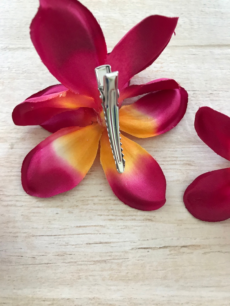 May include: A pink and yellow flower hair clip with a silver clip. The flower is made of fabric and has a realistic appearance.