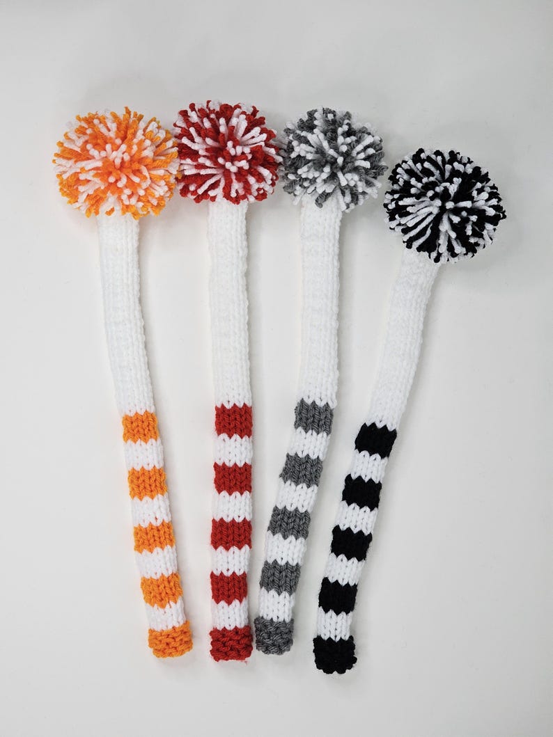 Puede incluir: Cuatro fundas para la cabeza de los palos de golf con pompones. Las fundas son blancas con rayas de color naranja, rojo, gris y negro.