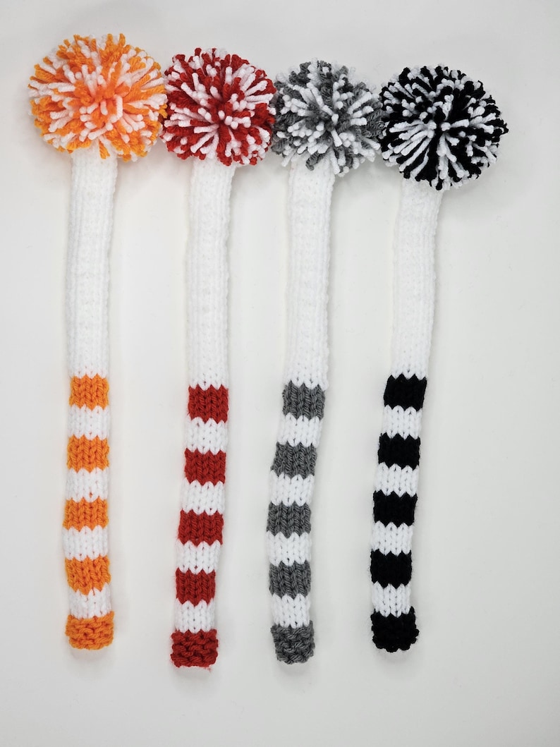 Puede incluir: Cuatro fundas para la cabeza de los palos de golf con pompones. Las fundas son blancas con rayas de naranja y blanco, rojo y blanco, gris y blanco, y negro y blanco.