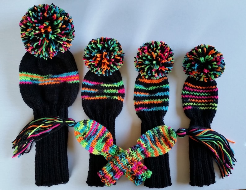 May include: A collection of black knit golf club head covers with vibrant neon stripes and pom-poms. The covers feature neon orange, green, and pink accents. The tassels at the bottom match the colorful design, offering a stylish accessory for golf enthusiasts.