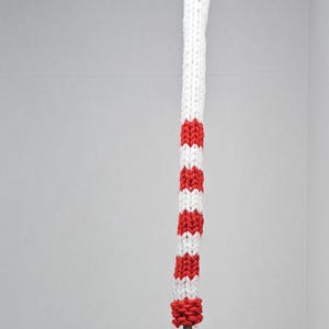 Puede incluir: Cubierta para la cabeza del palo de golf a rayas rojas y blancas con un pomp&oacute;n en la parte superior.