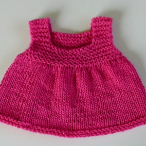 May include: A pink knitted sleeveless dress for a doll or small child.