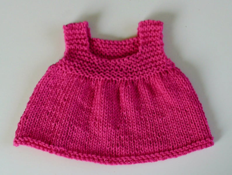 May include: A pink knitted sleeveless dress for a doll or small child.
