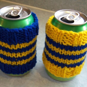 Może przedstawiać: Dwa aluminiowe puszki z napojami z dzianinowymi osłonami w niebiesko-żółte paski. Pokrowce są wykonane z przędzy i mają na celu utrzymanie napojów w chłodzie.