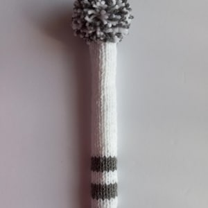 May include: A long, white knitted golf club head cover featuring a textured white and gray pom-pom at the top. The lower section of the cover displays three horizontal gray stripes against a white knitted background, creating a simple, clean design.